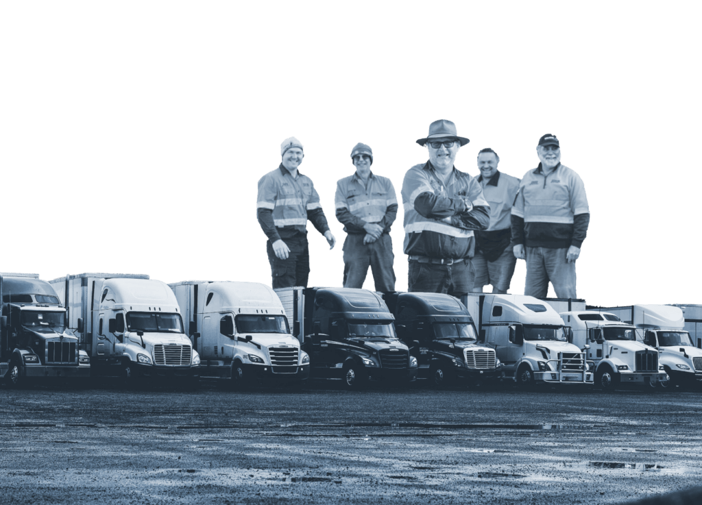 A team of truck drivers standing above their lineup of trucks parked in a gravel lot.